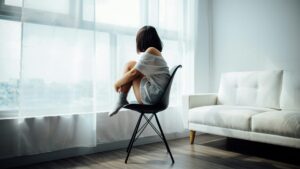 Foto Blog Trennung gründe: Eine Person allein auf einem Stuhl mit angezogenen Beinen vor einem Fenster